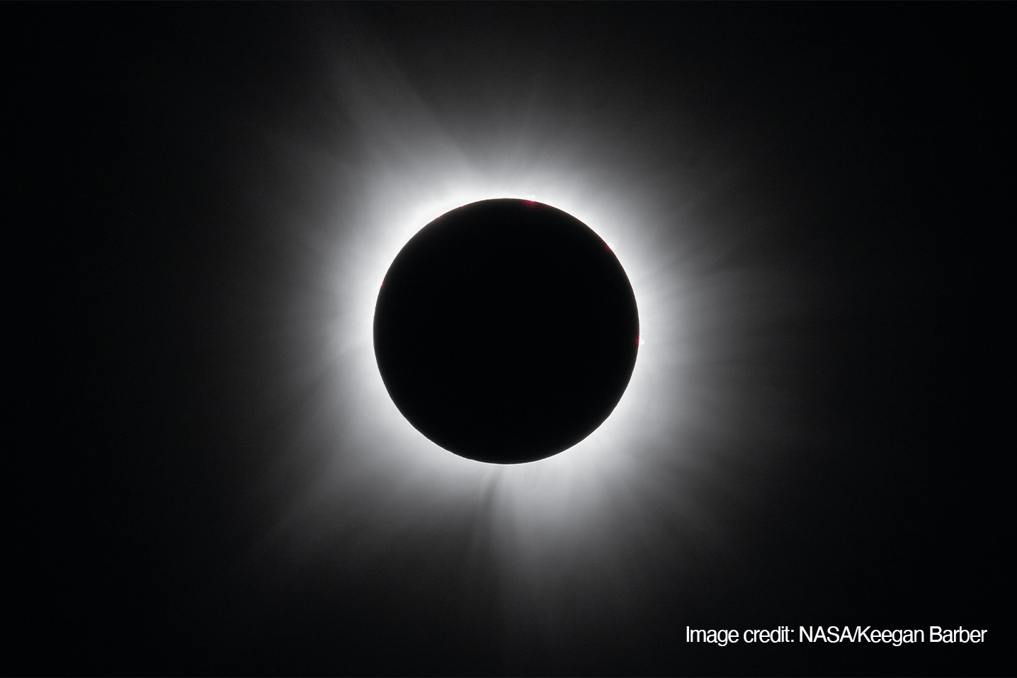A black disk appears in the middle of the photo with white rays radiating out from the circle, gently fading into the black background.