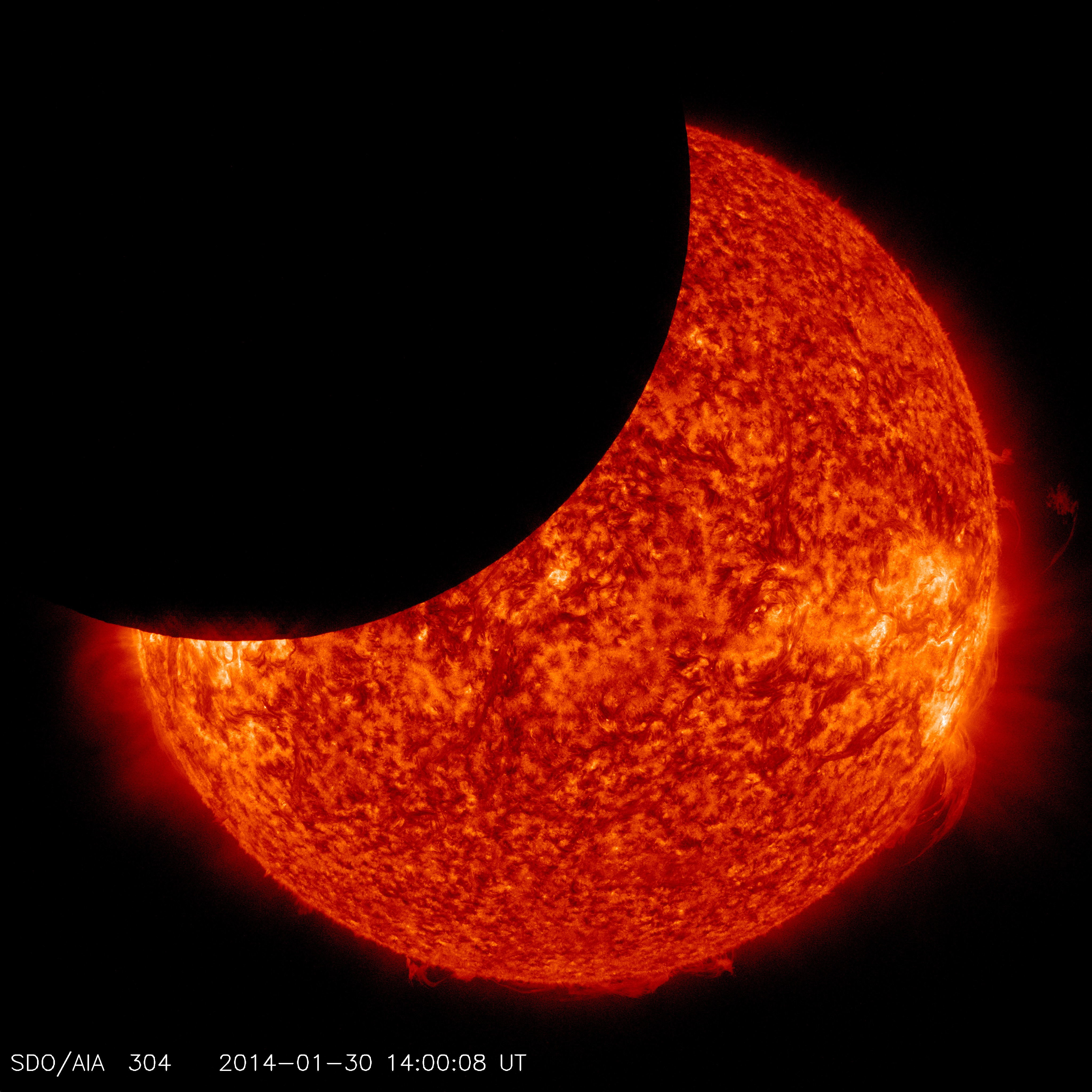 The Sun, seen in red with bright orange area, partially covered by black circle coming from the top left – the Moon.