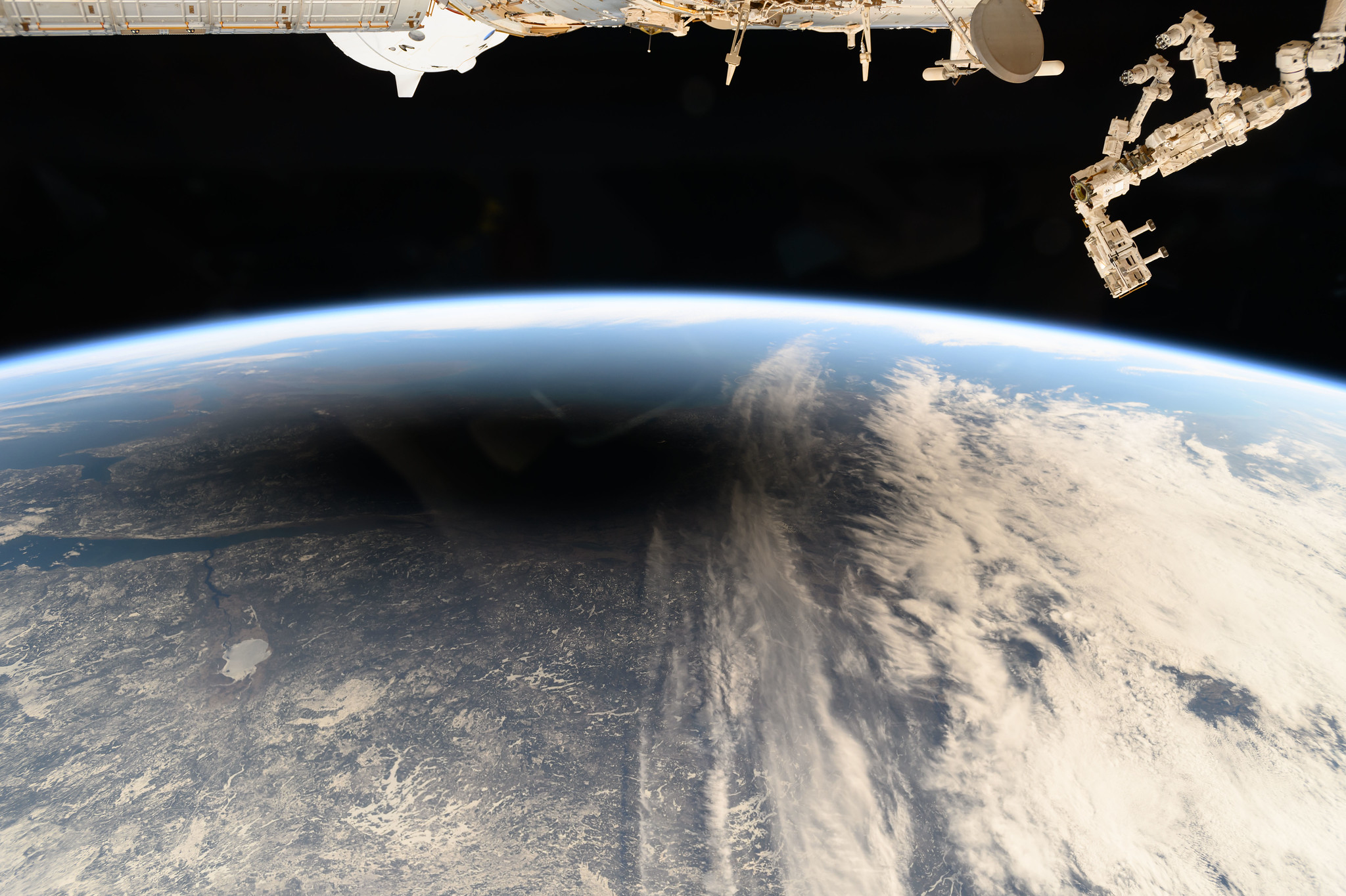A portion of the Earth seen from above, blue and partially covered with clouds. In one area is a very dark, black and gray circular shadow.