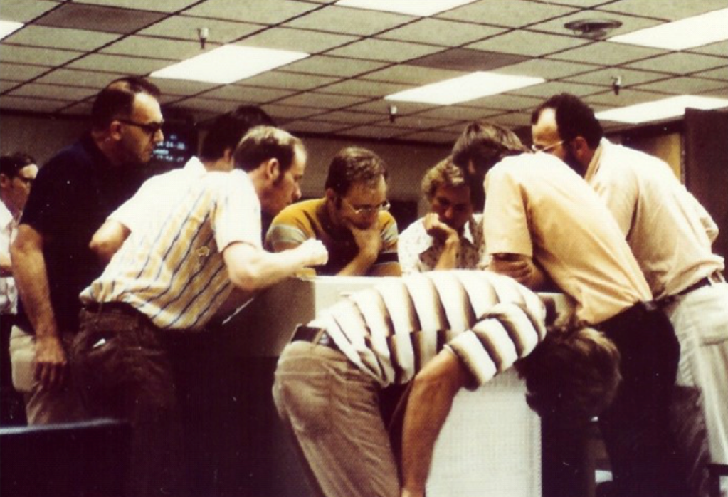 A group of men huddled around a table to look closely at something