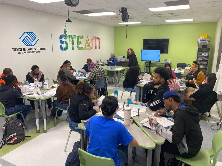 Lori Rubino-Hare guides a group of 20 out-of-school-time educators sitting in small groups to examine PLANETS printed materials at the Boys and Girls Club of Greater Houston STEAM lab.