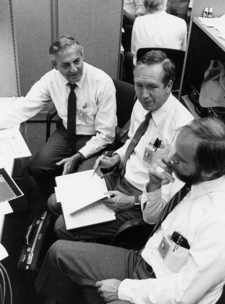 Three men discussing information on a notepad