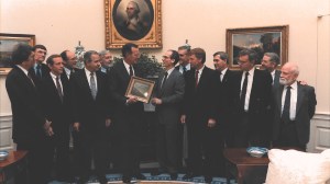 A group of men stand around President Bush as he receives a framed photo from a scientist.