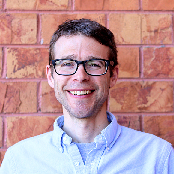 Kevin France headshot, male, brown hair, glasses, blue button down shirt, smile, faint stubble beard.