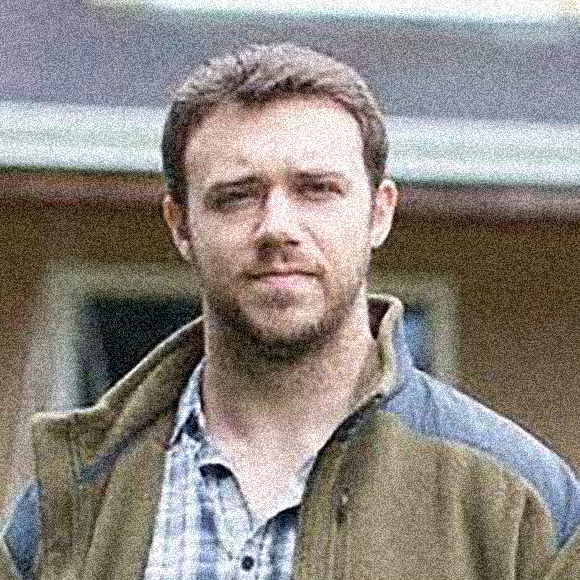 Tyler D. Groff headshot, brown hair, beard, plaid button-down shirt, brown fleece jacket.