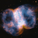 Taking up most of the image, is a multi-colored nebula in shades of blue, pink, yellow, orange, purple, and white. It appears as two translucent orbs attached by a white band.