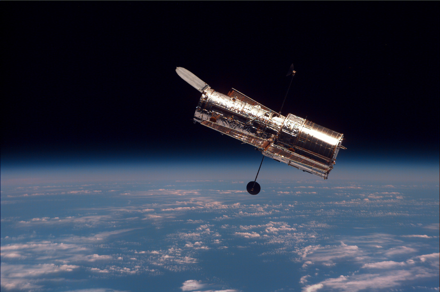 Hubble floats above a blue Earth streaked with clouds.