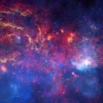 A colorful view of the Milky Way's center region. Colors of red, orange, yellow, blue, pink, and white are stars, clouds, and filaments against a dark backdrop.