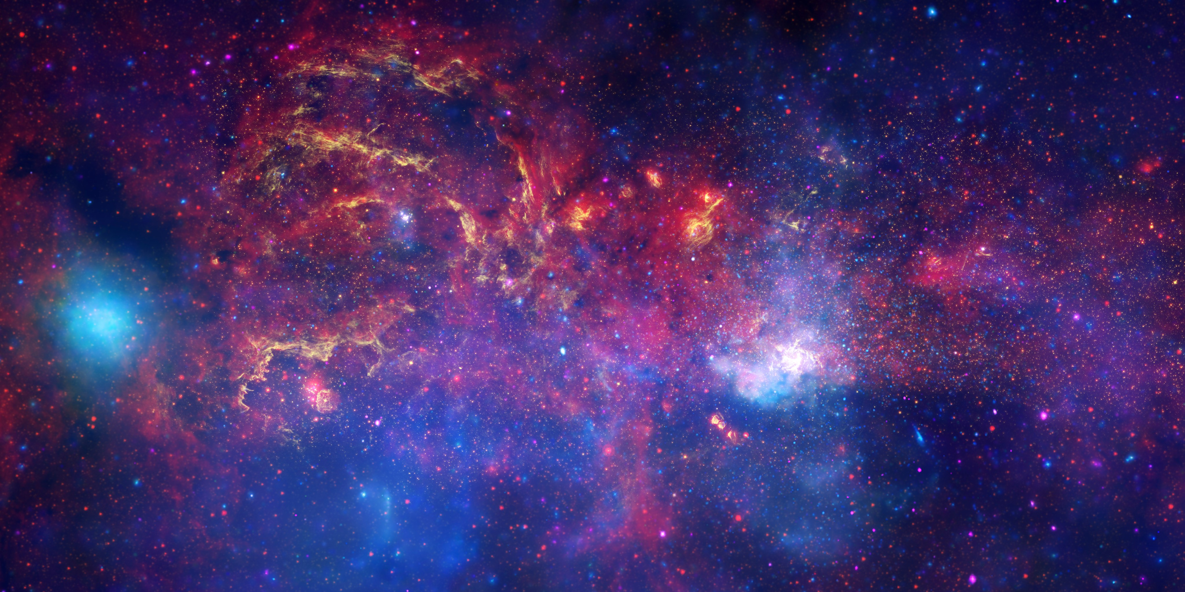A colorful view of the Milky Way's center region. Colors of red, orange, yellow, blue, pink, and white form clouds and filaments against a dark backdrop.