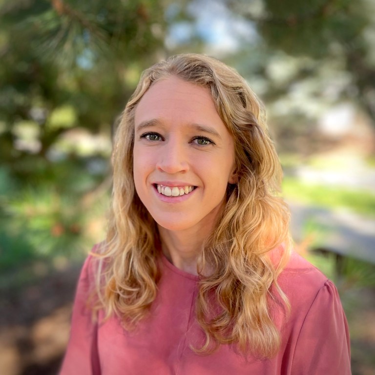 Briana Indahl headshot, female, blonde wavy hair, pink shirt, smile.