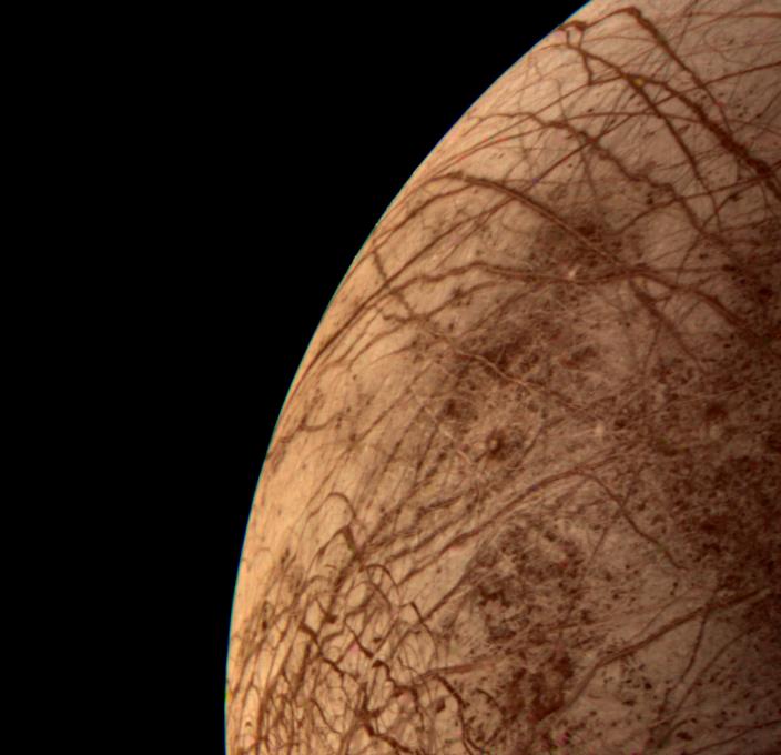 Criscrossing lines and squiggles mark the reddish surface of Europa.