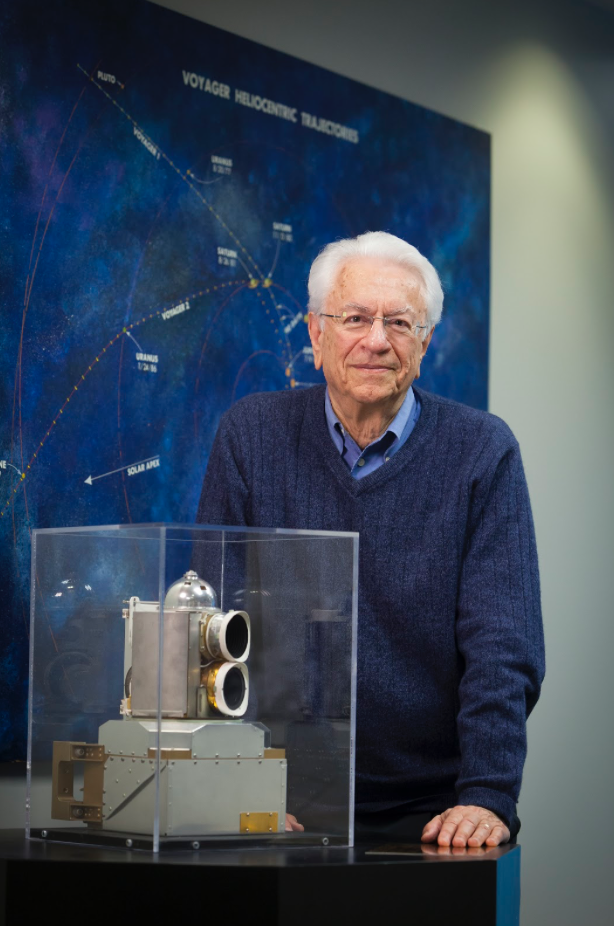 Stamatios (Tom) Krimigis standing next to a camera or instrument inside of a glass case