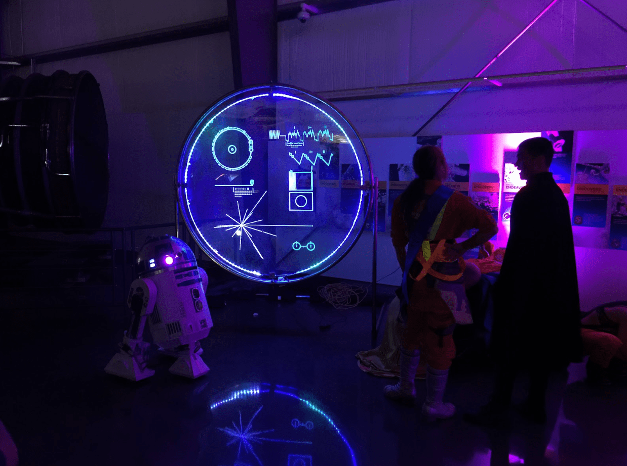 People in a dark room staring at a light projection of the symbols on the Voyager Golden Record cover