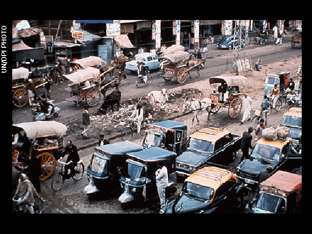 A crowded street with early 20th-century cars and horse-drawn carriages