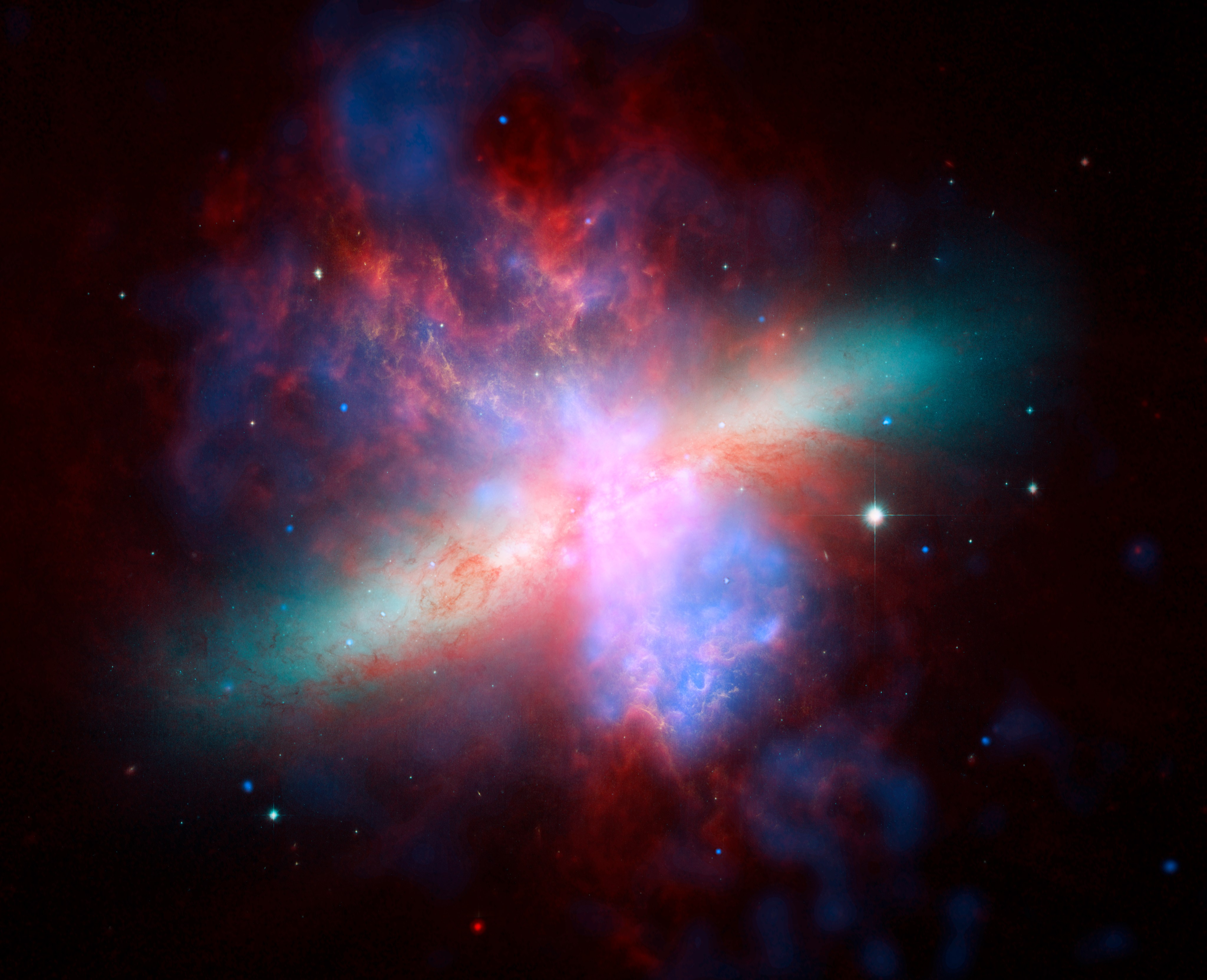 美国国家航空航天局的斯皮策、哈勃和钱德拉空间天文台联合制作了这张M82星系的多波长视图。这幅生动的肖像画庆祝了哈勃“甜蜜的十六岁”生日。钱德拉记录的X射线数据显示为蓝色；斯皮策记录的红外光呈红色；哈勃对氢发射的观测结果显示为橙色，最蓝的可见光显示为黄绿色。