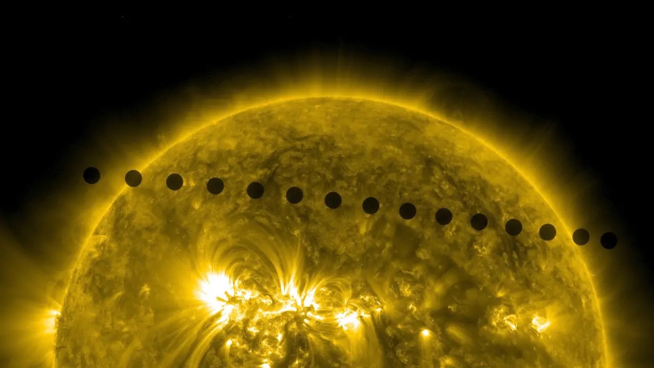 A composite of images of the Venus transit the fiery yellow glow of the Sun. The Venus images extend in a downward straight line at the top of the Sun. Venus appears as a small black dot.