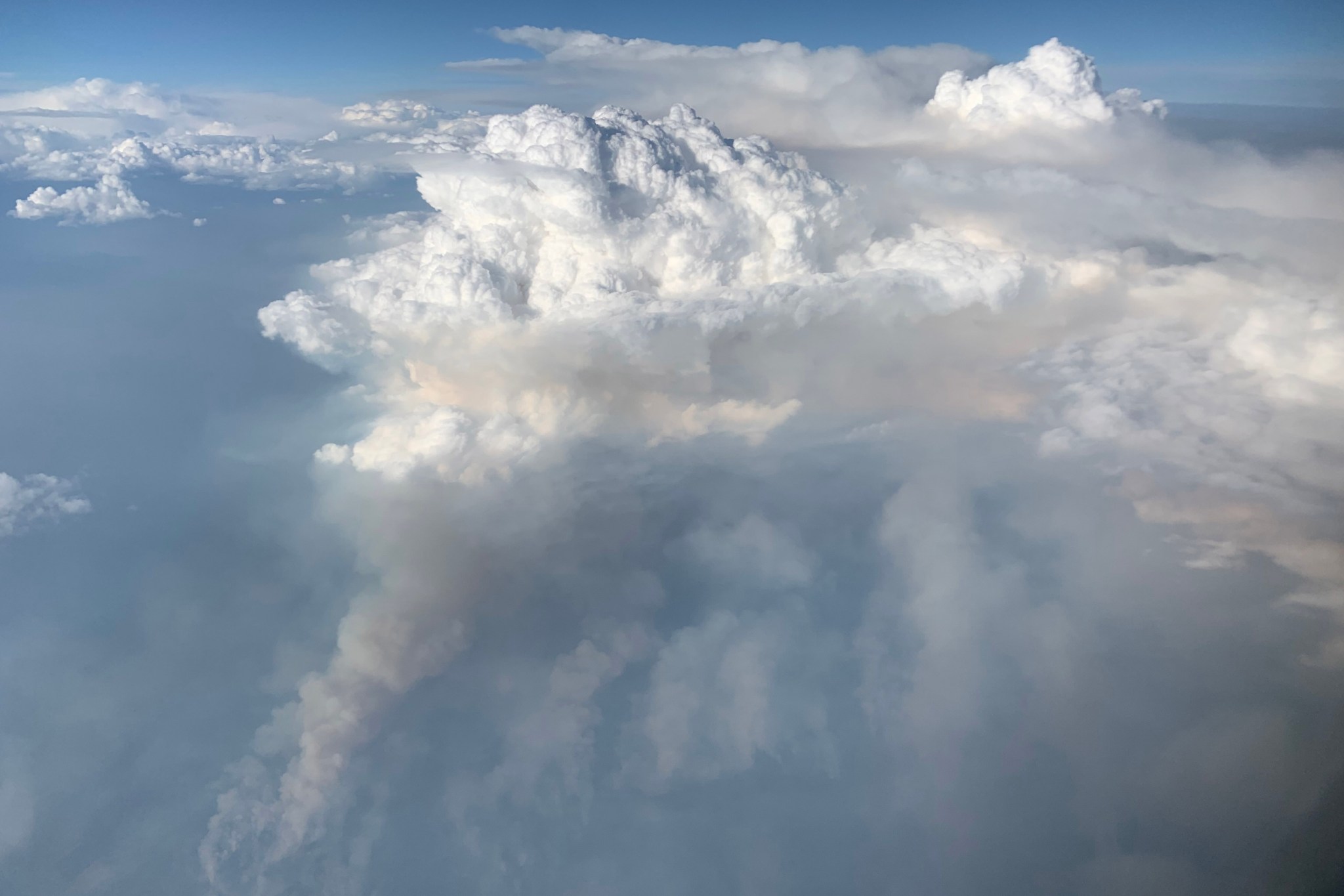 Image of a large white cumulus cloud rising above the average atmospheric clouds surrounding. The cloud has apparent columns attaching it to the ground below.