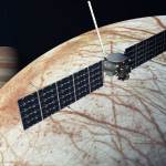 A spacecraft hovers over a reddish striped moon with planet Jupiter in the background.