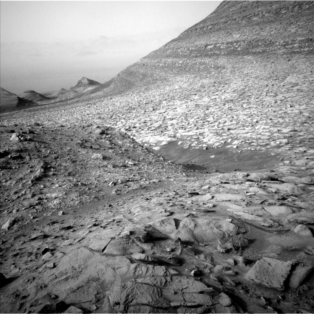 Image taken by the Mars rover Curiosity of a bumpy terrain of Mars. The image shows a hillside and a few vallies afar.