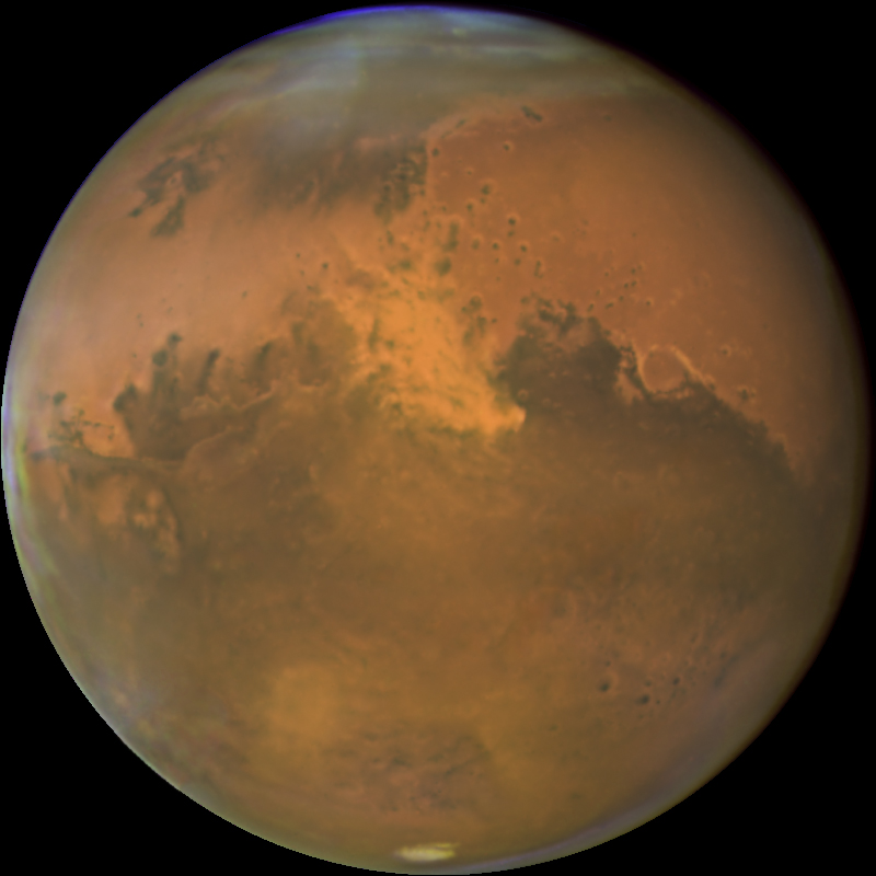 Rusty-red Mars is mottled with grey-brown regions in the Northern and Southern Hemispheres of the planet. Clouds are visible at the planet's North Pole, partially obscuring its north polar ice cap. The South Pole's ice cap is visible at the bottom of the image.