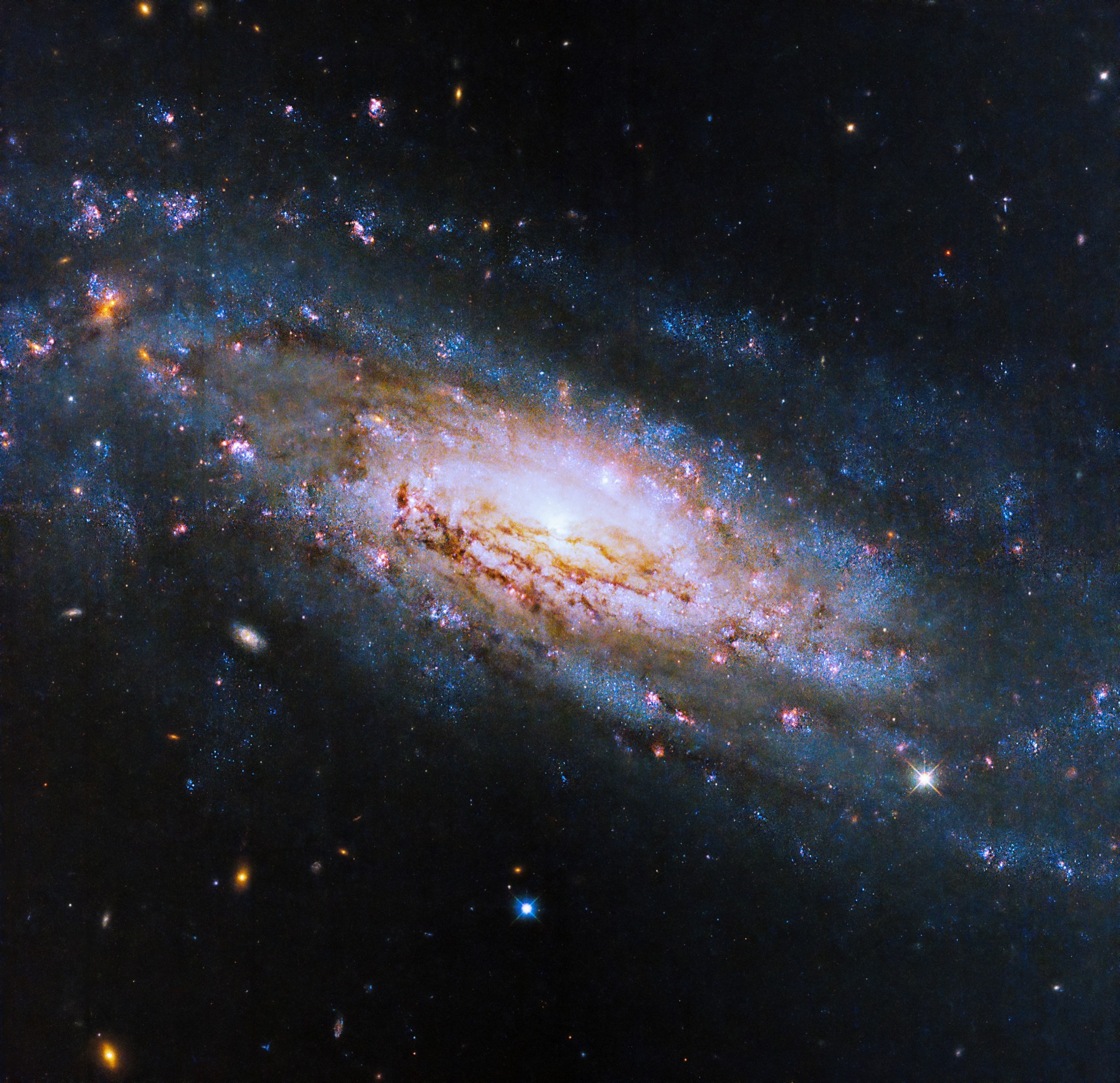 A massive spiral galaxy fills the image. A bright, yellow galactic core glows at the center, surrounded by spiral arms studded with pink stars and dark lanes of dust.