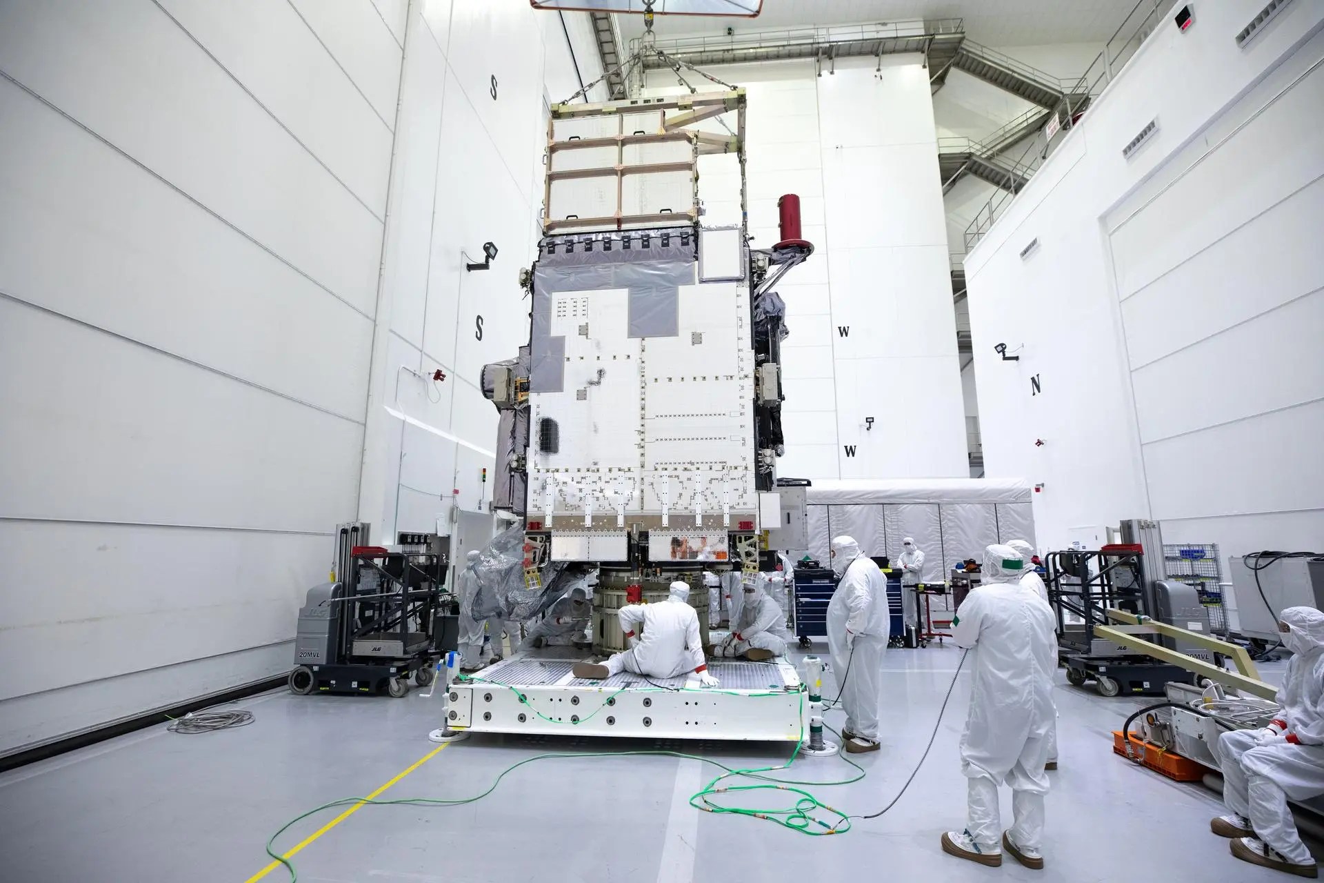 Image shows technicians in 'bunny suits' working on a GOES satellite in a clean room.