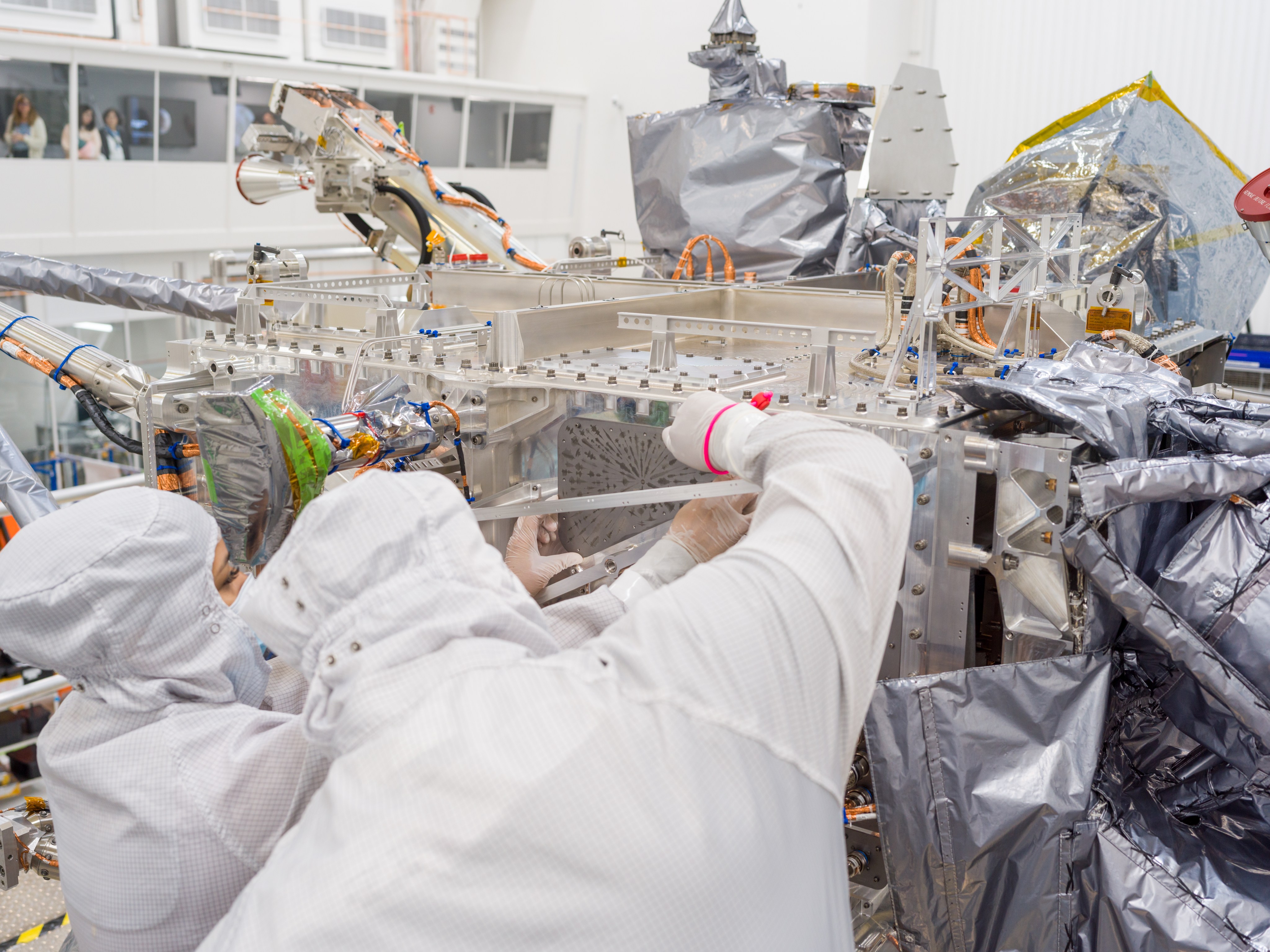 Two technicians in white protective clothing hold the Europa Clipper Vault Plate as they position it for installation on the spacecraft.