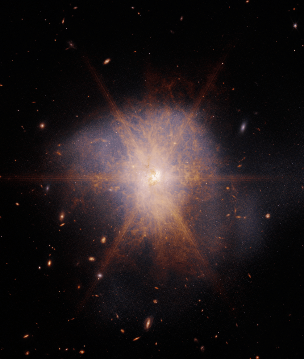 A black, deep space image is dominated by what appears to be a large snowflake-like feature with a bright white core and 8 pinkish orange spikes. It is surrounded by additional wisps of pinkish orange and blue gas.