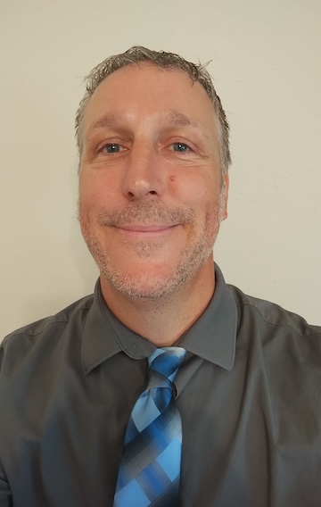Aaron Burton headshot. He is smiling in a dark gray shirt and blue tie.
