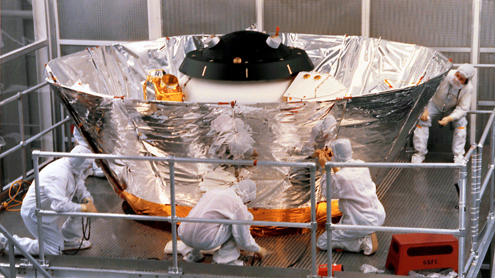 White-suited figures work on the COBE spacecraft.