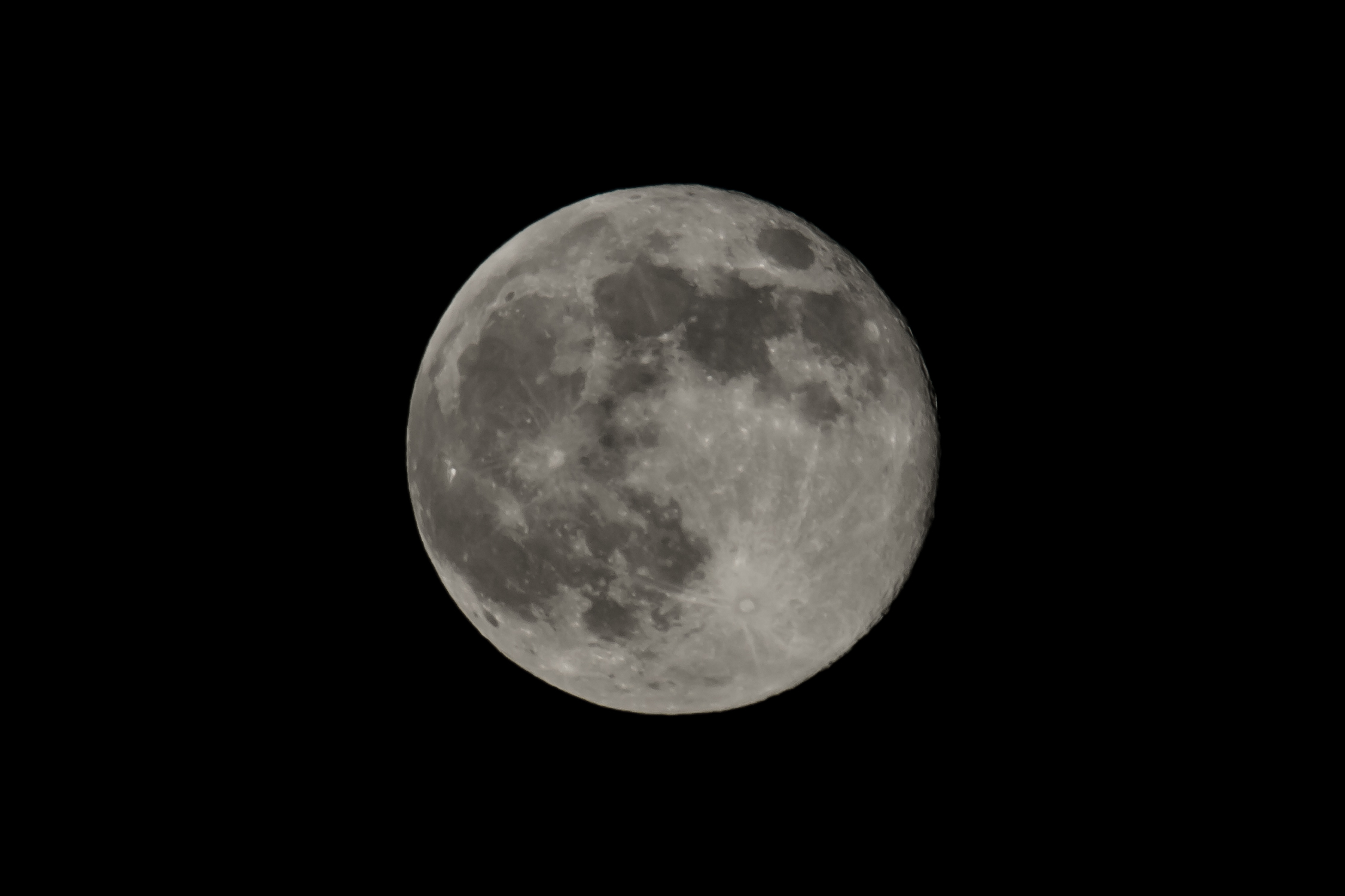 A gray Moon dotted with its darker maria against a black background.