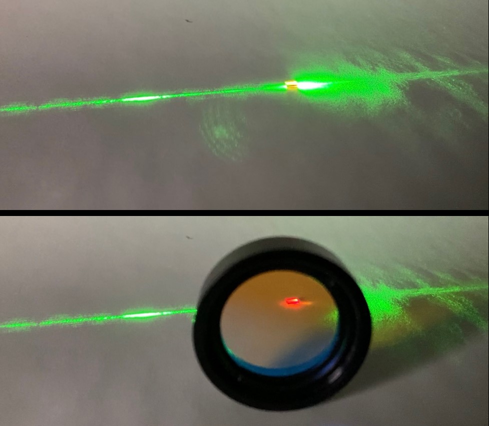 A bright green laser beam is hitting a tiny glassy cube. The bottom photo shows the same setup, but with a large circular filter added in front of the glassy cube. The laser beam is invisible behind the filter, the glassy cube emits a reddish glow.