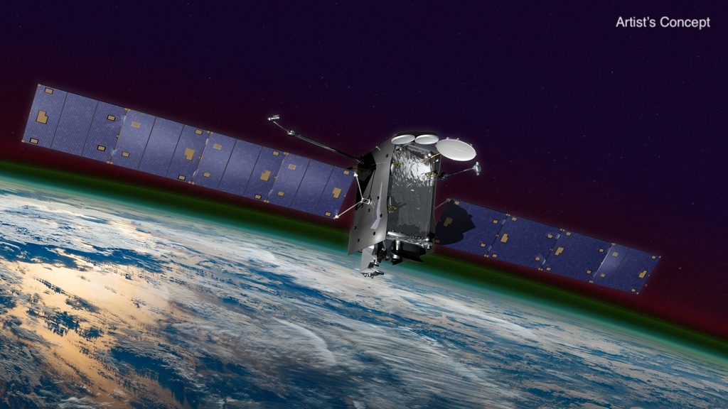 In the background, the bottom half of the image is filled with a portion of Earth. The top half is the very dark blue of space. Separating the two are bands of glowing greens and red, depicting the upper layers of Earth's atmosphere. In the foreground, a satellite. The satellite has two rectangular wing-like structures jutting out from the right and left of a silver rectangular box. On the top are 3 large white dishes.