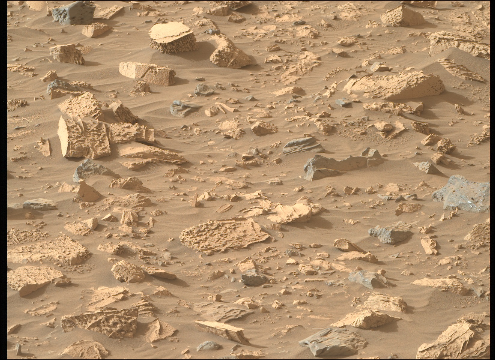 Rocky, pale-orange-colored terrain on Mars. What looks like fine-gran sand is interspersed with many jagged rocks pointing out of the ground; a few of the rocks are gray, not orange.