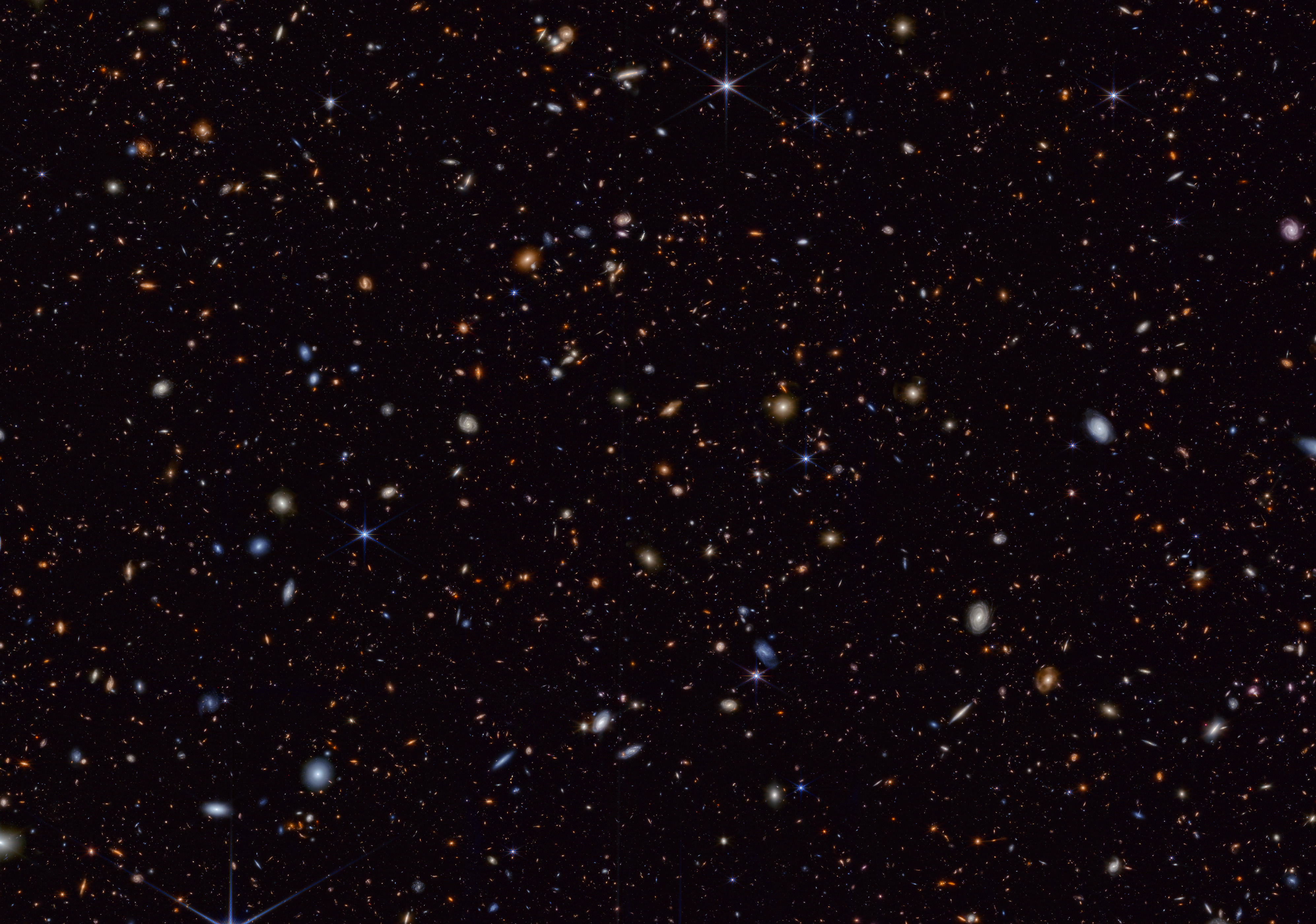 Webb Space telescope deep field image showing hundreds of objects of different colors, shapes, and sizes scattered across the black background of space.