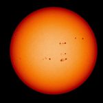 An image of the Sun. The Sun is yellow and orange and speckled with several dark splotches – sunspots.