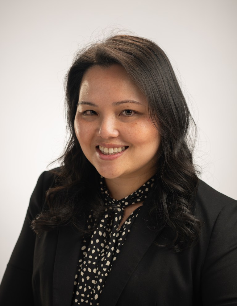 Studio portrait of Diana Ly. She's smiling and has long dark hair. She's wearing a black jacket, black and white neckerchief, and a black and white top.