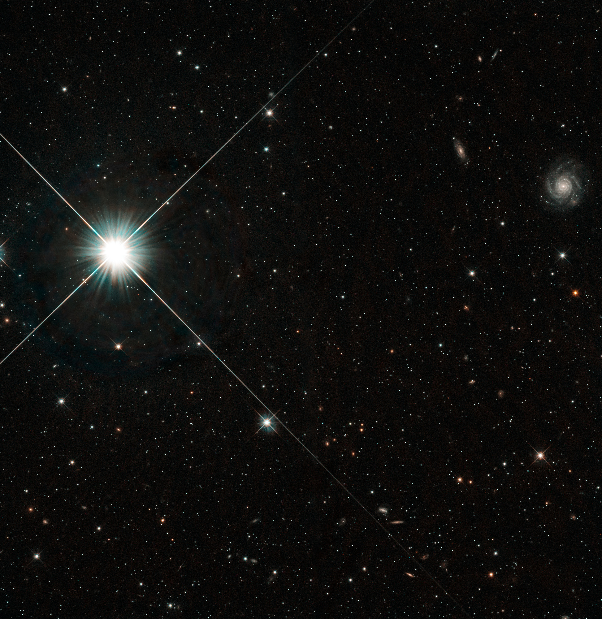 Distant and nearby galaxies dot an inky-black background. Bright foreground stars hold four diffraction spikes.