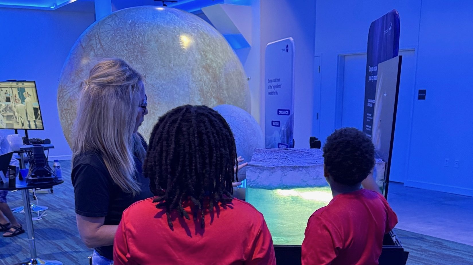 A NASA public engagement specialist points to part of an exhibit showing Europa's shell and ocean.