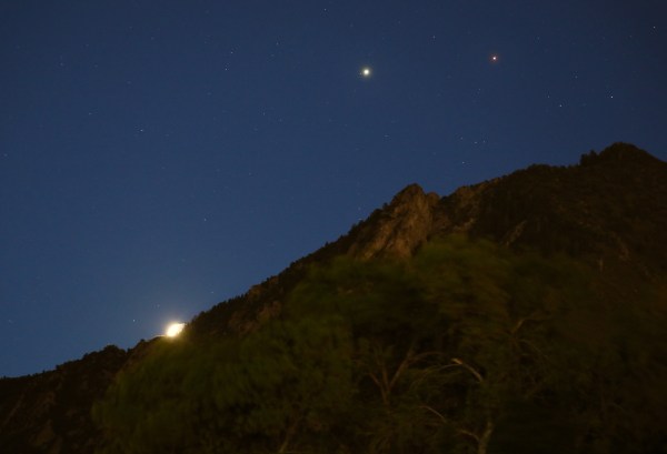 Jupiter and Mars shine high above a mountain ridge. The Moon is peeking over the top ridgeline.