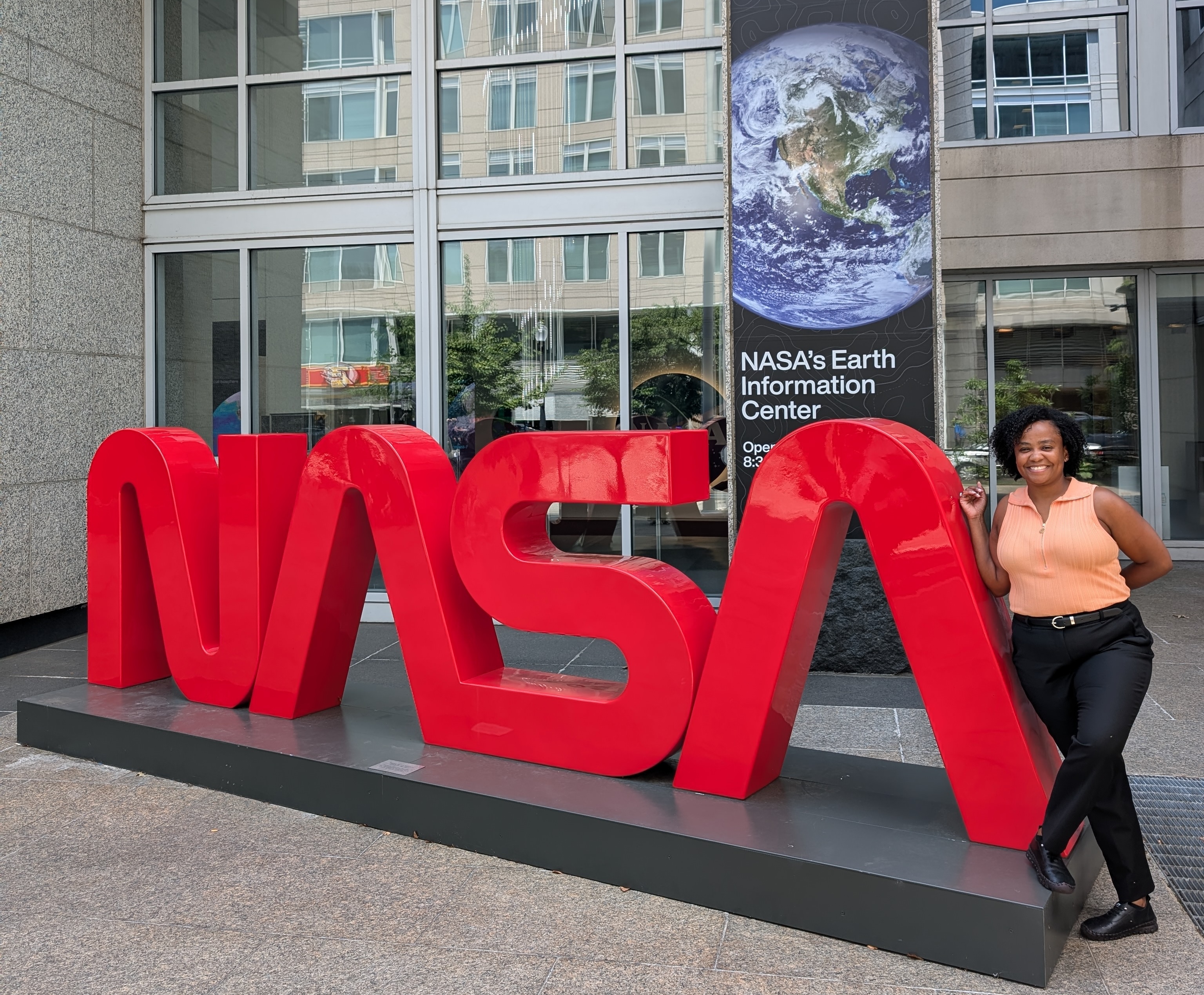 NASA intern Lena Young leans against a red NASA sign in front of NASA's Earth Information Center.