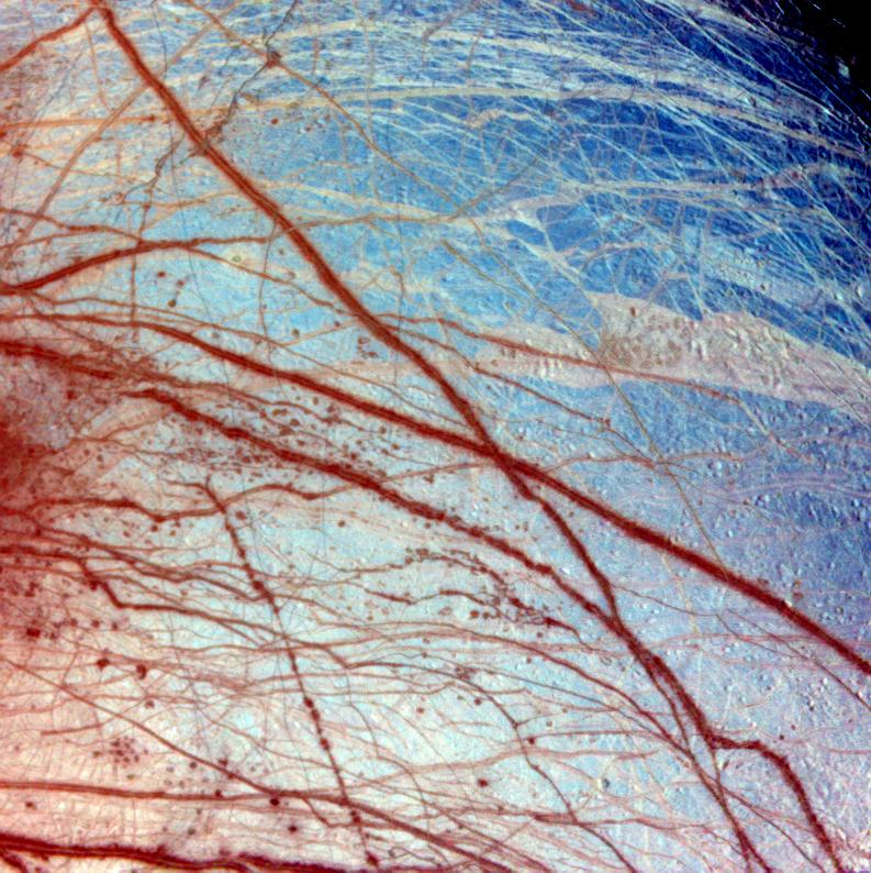 A color enhanced photo of Europa showing a bluish surface with reddish streaks.