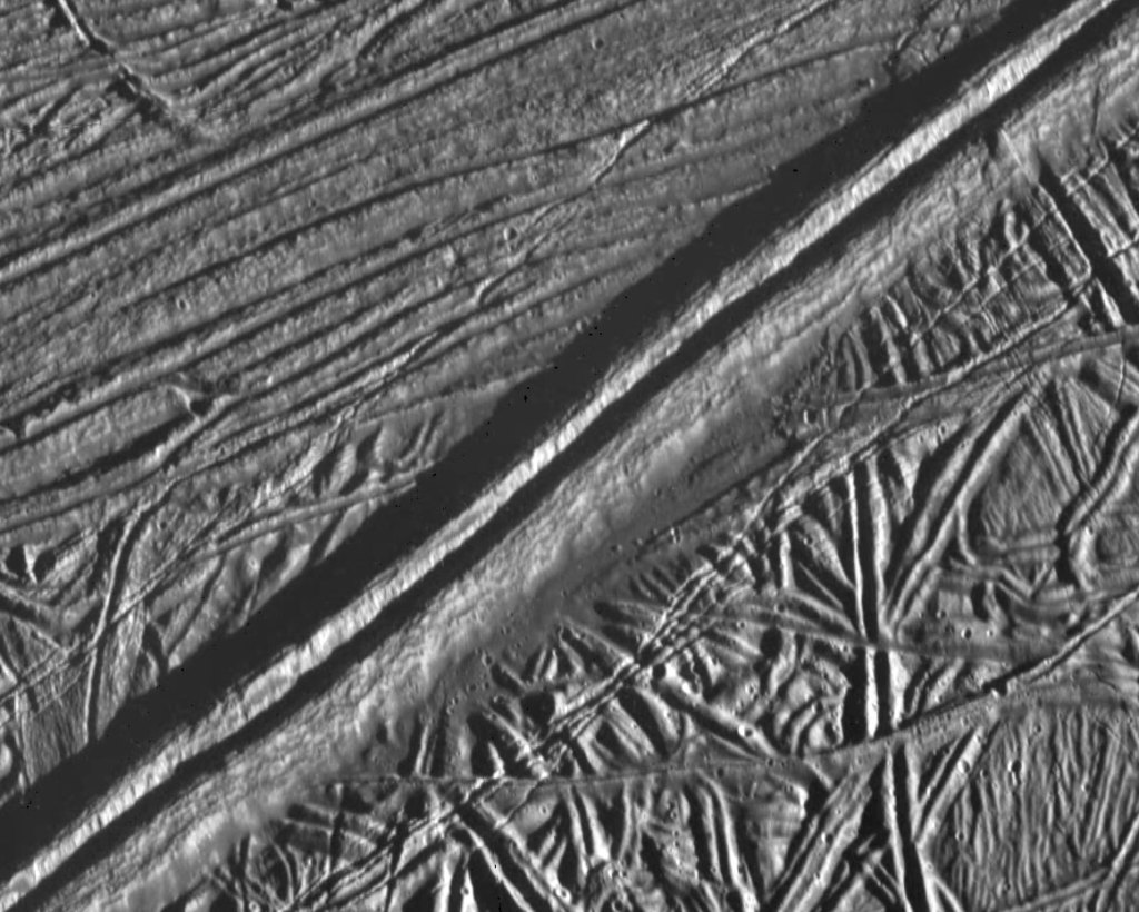 In this close-up image, Europa's surface appears gray with a ridge cutting across the middle of it.