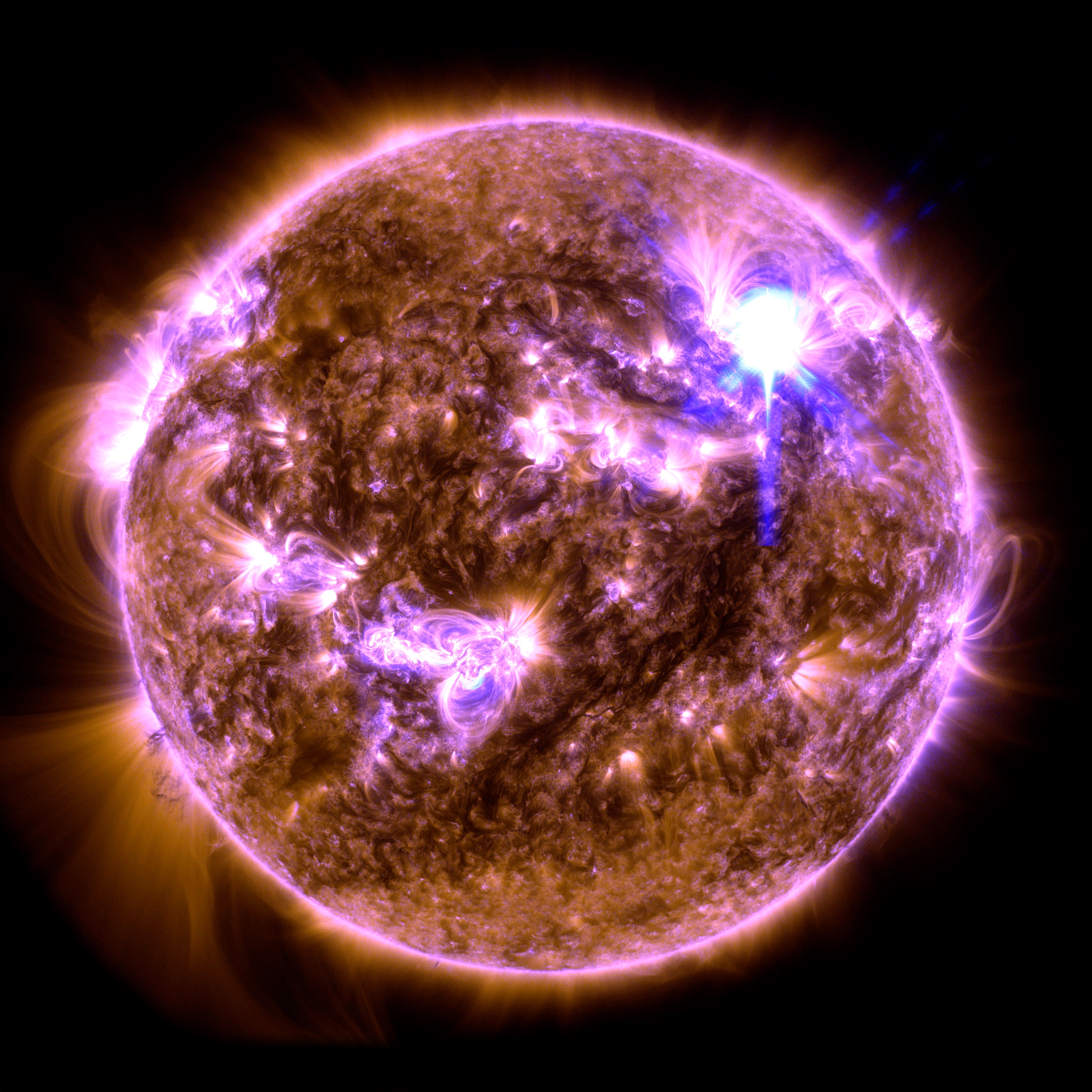 The Sun appears as a mottled orange orb, with several bright regions of swirling plasma appearing in pink and purple. A bright white flash of light appears in the upper right.