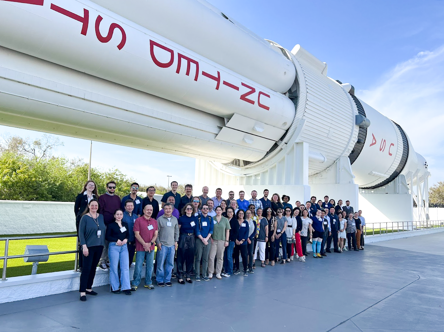 A group of people standing in front of a SATERN V rocket at the TOPS Open Science Symposium