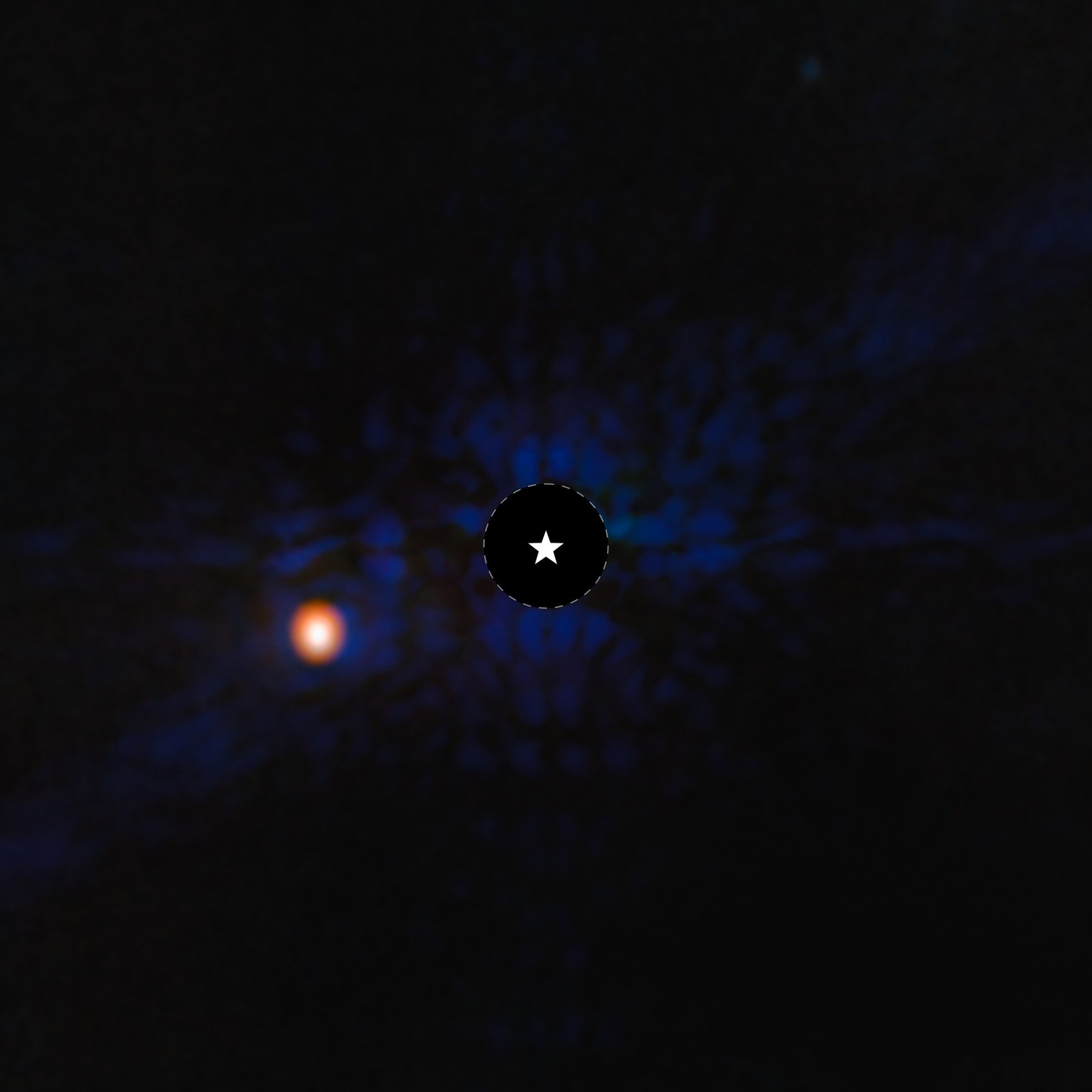 This image shows the exoplanet Epsilon Indi Ab. The image is mostly black, with blue scale-like features apparent in the central region of the image. At the center of the image, there is a black circle, and in the center, a symbol representing a star. This black circle blocks the light from the host star. To the lower left of the circle is a fuzzy bright orange circle, which is the exoplanet.