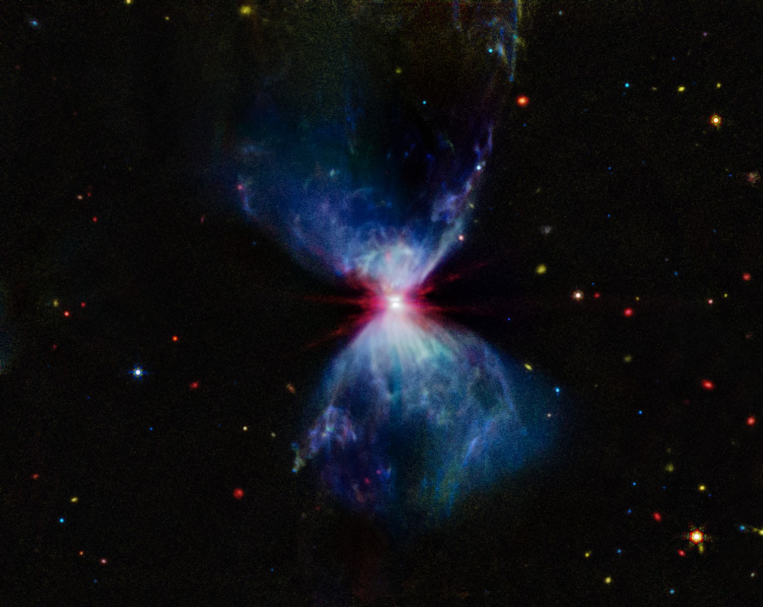 A growing protostar embedded within a molecular cloud. The center of the image shows a bright, red region, where the growing protostar resides, with a thin, gray lane of matter cutting through it horizontally, which is the protostar's accretion disk. Above and below this region are blue triangular-shaped molecular clouds, which give the overall object an hourglass shape. The areas in the molecular clouds closest to the protostar have more pronounced plumes of blue gas. There are red, yellow, orange, blue, and green stars and galaxies scattered across the background.