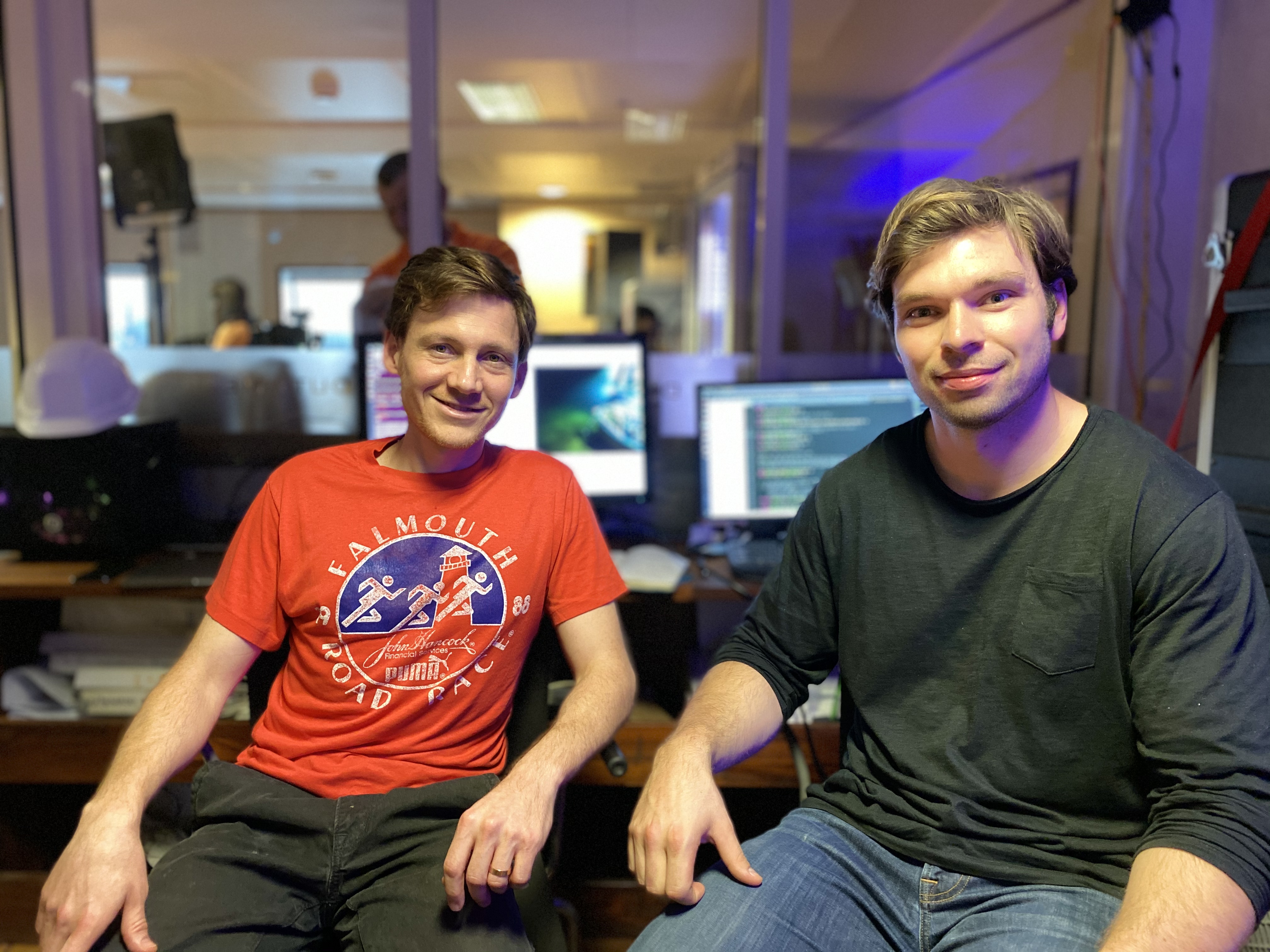 Two male researchers sit in front of monitors in the ship's control room.