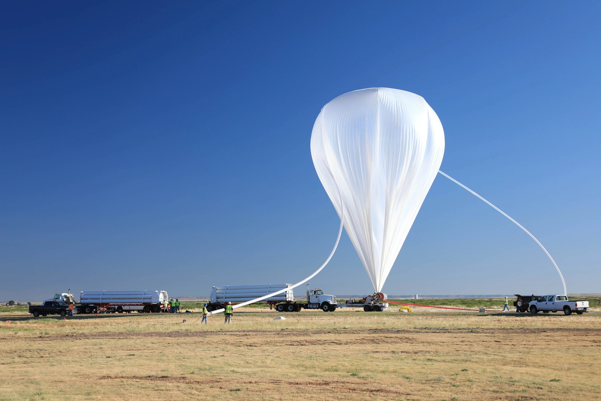 A white scientific balloon is tethered to the ground before launch.