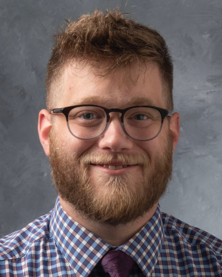 Portrait of a smiling, bearded man wearing glasses, dress shirt, and tie.